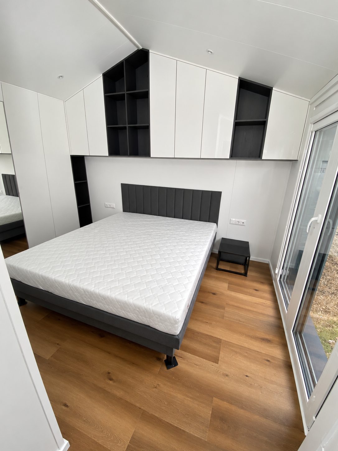 Schlafzimmer im Modulhaus Diamond +Plus Deluxe ATB-62 mit Doppelbett 180 × 200, Polsterkopfteil und Einbauschränken.